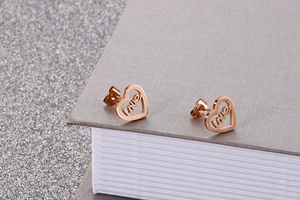 Macro shot of rose gold heart stud earrings featuring love engraving on fabric