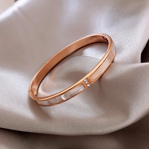 Rose gold stainless steel shell bangle with crystal accents on a silk background
