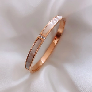 Detailed shot of rose gold shell bangle with three zircons on white silk fabric