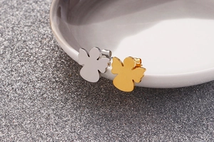 Detailed macro view of gold and silver angel-shaped stainless steel stud earrings on ceramic