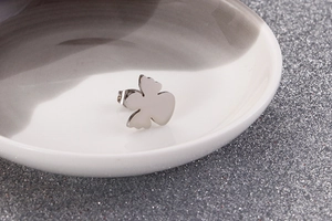 Macro view of a silver bear-shaped stud earring on a gray glitter background