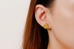 Close-up of gold four-leaf clover stud earrings with small diamond on female model