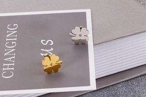 Macro view of minimalist clover stud earrings in gold and silver steel finishes