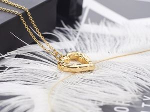 Macro shot of textured golden heart pendant resting on white feather and gift box