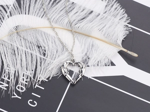 Detailed shot of silver heart wing pendant on white feathers with metal gloss
