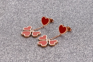 Detail of rose gold clover earrings with red heart enamel charms on glitter background