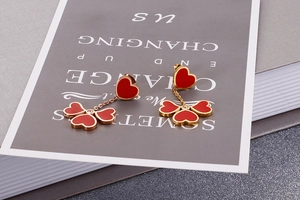 Macro detail of red enamel heart and leaf earrings on a grey card with gold accents