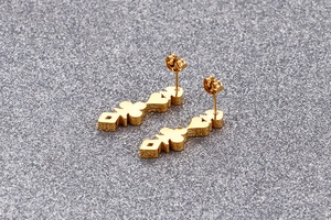 Dettaglio di orecchini a cerchio dorati con ciondoli geometrici a cuore e picche in oro