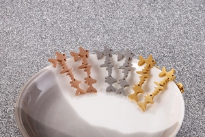Three-color stainless steel fish heartbeat stud earrings on white ceramic plate rim