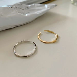 Irregular wavy rings in gold and silver finish shown next to luxury hand cream
