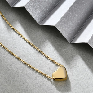 Detail of 18K gold heart pendant on stainless steel chain over stone texture