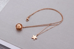 Detail of rose gold necklace featuring star and circular pendants on a notebook surface