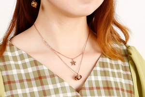 Detail view of rose gold layered necklace and star earrings set worn by a model