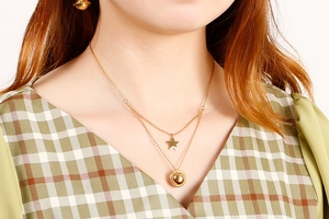 Close-up of a double-layered gold star and bead pendant necklace worn by a model