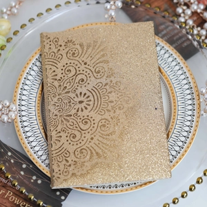 Detail of laser-cut glitter wedding invitation with intricate lace pattern in gold finish