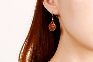 Close-up of a gold-plated flower drop earring with red enamel camellia pattern on a model
