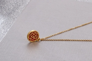 Close-up of golden necklace with a circular rose pattern pendant and red inlay