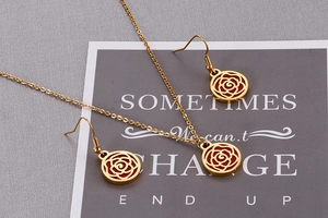 Detail of gold hollow rose jewelry set with red inlay on a grey textured background