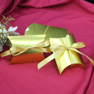 Drei goldene kissenförmige Geschenkschachteln mit passenden Seidenbändern auf dunkelrot