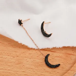 Detalle de pendientes asimétricos oro rosa con pavé de luna y estrella negras