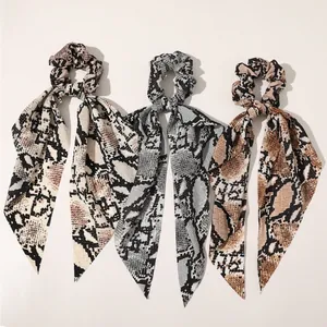 Close-up of three satin bow scrunchies featuring trendy snakeskin patterns in various colors