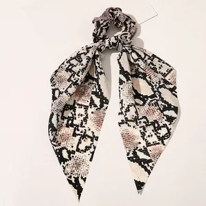 Macro shot of snakeskin print satin hair scrunchie with long ribbons on white surface