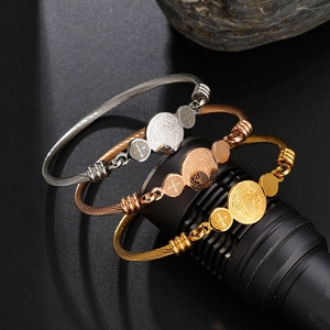Detailed macro view of three-tone stainless steel cable bracelets with St. Benedict medals