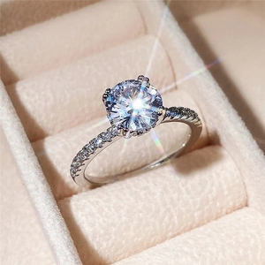 Classic round solitaire engagement ring with pave side stones on a beige velvet box