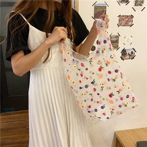 Detailed close-up of colorful floral embroidery on a white mesh tote bag held by a person