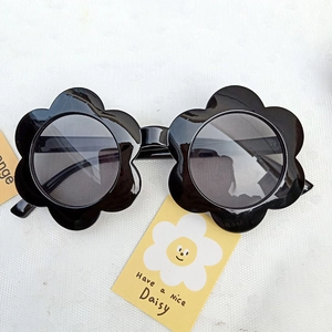 Flat lay of black daisy-shaped flower sunglasses for toddlers on a decorative white card