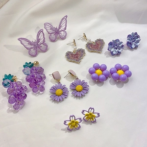 Flat lay of purple floral and butterfly earrings on white silk fabric background