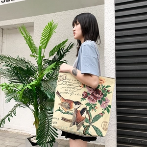 Close-up of beige canvas tote bag with floral bird embroidery and shoulder strap
