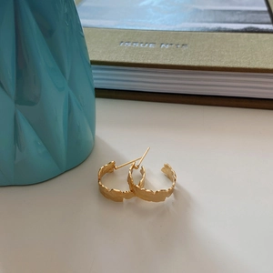 Detail view of irregular textured gold earrings with metallic hammered finish in a still life