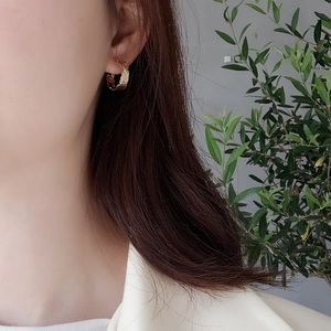 Close-up of golden irregular textured hoop earring worn on earlobe with plant background