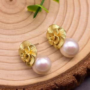 Macro detail of natural pearl earrings featuring gold flower petals and white round pearls