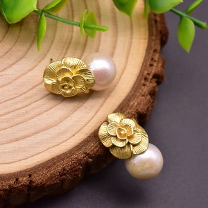 Macro detail of golden rose earrings with round white pearls on a natural wood surface