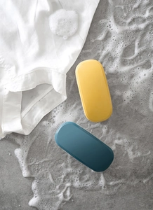 Close-up of yellow and blue plastic laundry brushes on a soapy grey surface with a white shirt
