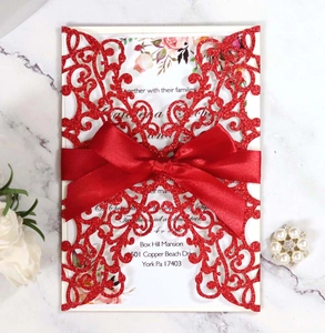 Detail of red laser-cut wedding card with satin bow and floral inner page on marble