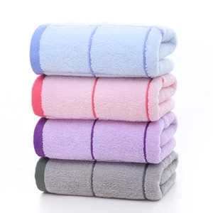 Close-up of four stacked cotton towels in blue, pink, purple, and gray with stripe pattern