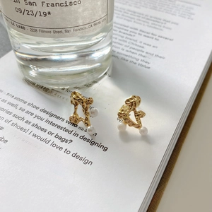 Close-up of gold irregular texture earrings with pearls on a book with perfume background