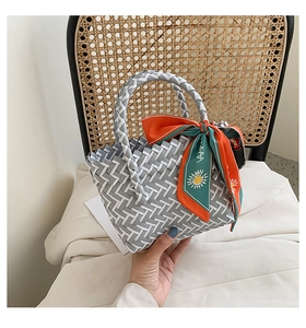 Detail of grey and white woven tote bag with daisy ribbon on a rattan chair