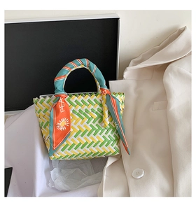 Detail of woven straw bag in green, yellow, white with decorative patterned silk scarf