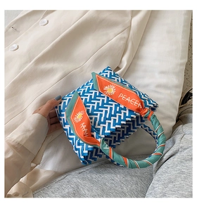 Detail of blue and white woven basket bag with chic orange solar print silk scarf handle