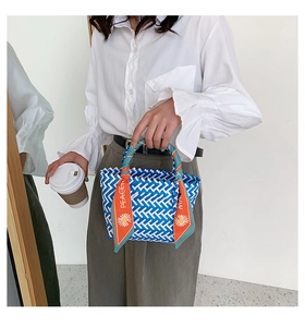 Close-up of blue and white woven tote bag with orange peace silk scarf on the handle