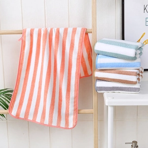 Détail de serviettes en polaire corail à rayures orange, bleu et gris sur un support en bois