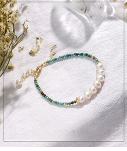 Detail of turquoise and freshwater pearl bracelet with golden clasp on white fabric