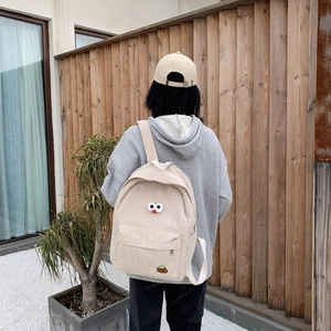 Mochila de pana beige con ojos de dibujos animados usada por una modelo en un estilo informal