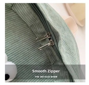 Close-up detail of smooth double metal zippers on the light green corduroy backpack