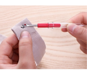 Close-up of a red seam ripper picking stitches on purple fabric over a wooden surface