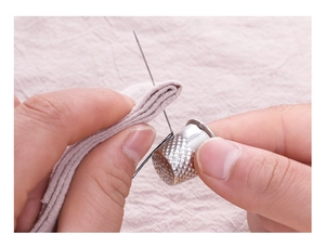 Macro shot of a silver metal thimble protecting a finger during sewing on purple fabric